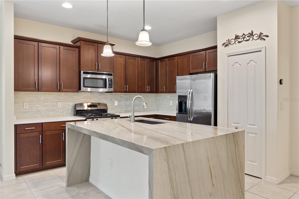 Gourmet kitchen featuring quartz counter tops, ample cabinetry, a large island with waterfall edge, and stainless steel appliances.