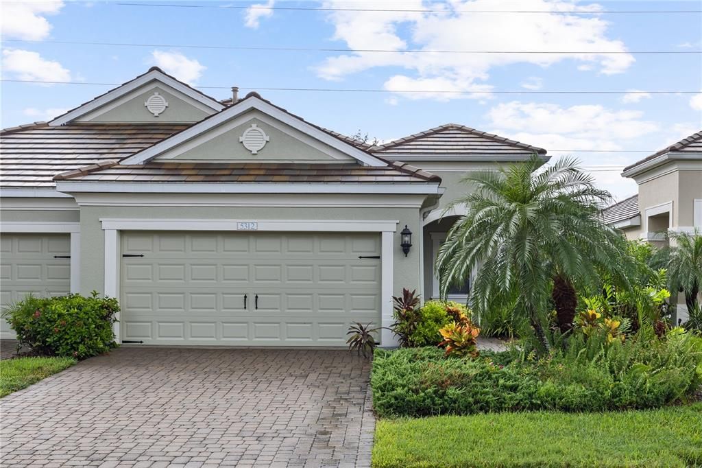 Front Elevation showing the paver driveway, tropical landscaping, and front porch.