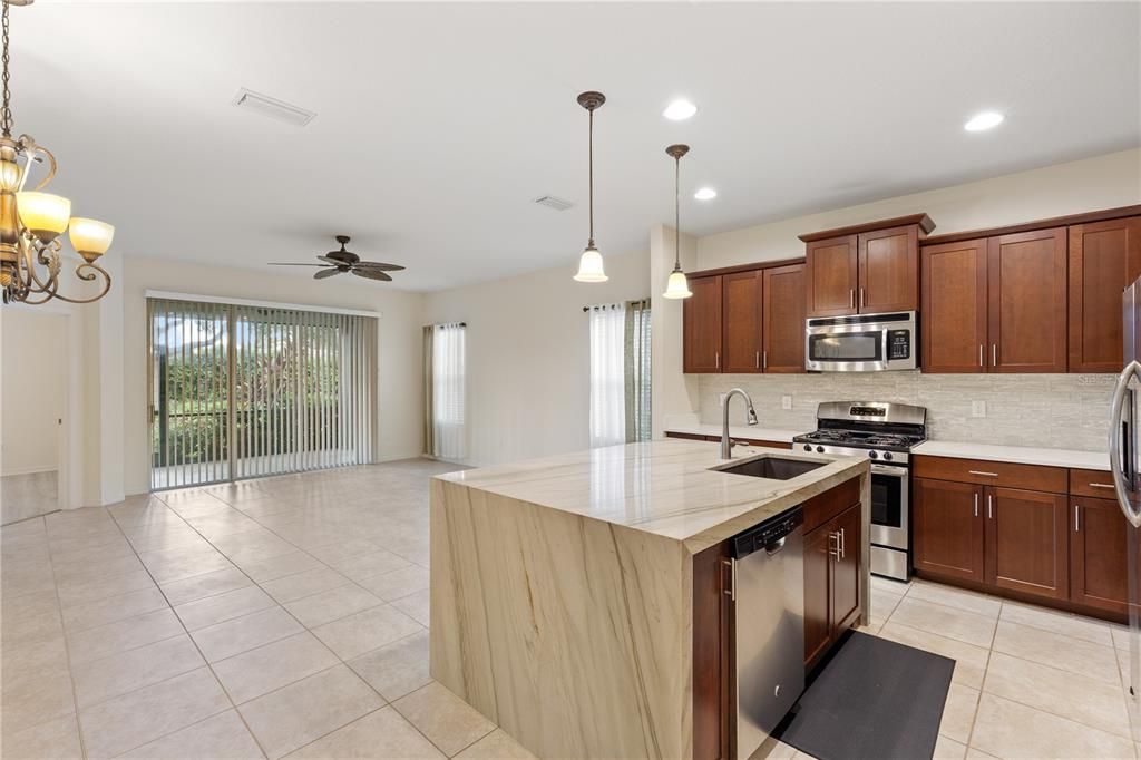 Gourmet kitchen featuring quartz counter tops, ample cabinetry, a large island with waterfall edge, and stainless steel appliances.