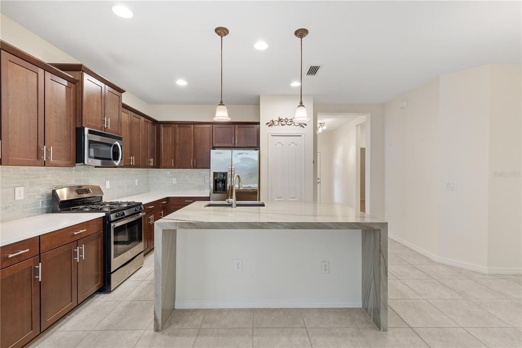 Gourmet kitchen featuring quartz counter tops, ample cabinetry, a large island with waterfall edge, and stainless steel appliances.