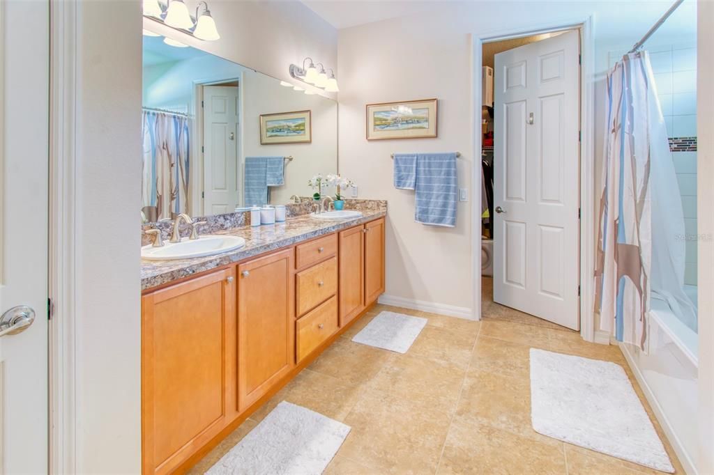 The fist primary bath is luxurious has a large vanity, drop mounted sinks, gleaming wall tile with a glass listello inset around the soaking garden tub with shower, with transom window above - beyond is a large walk-in closet