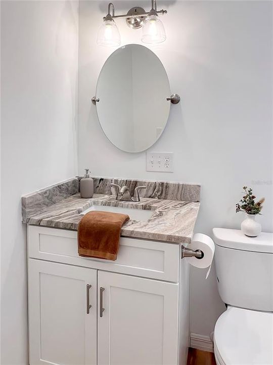 Bathroom featuring new white shaker vanity with granite countertops, toilet, mirror, light fixture, LVP flooring and paint