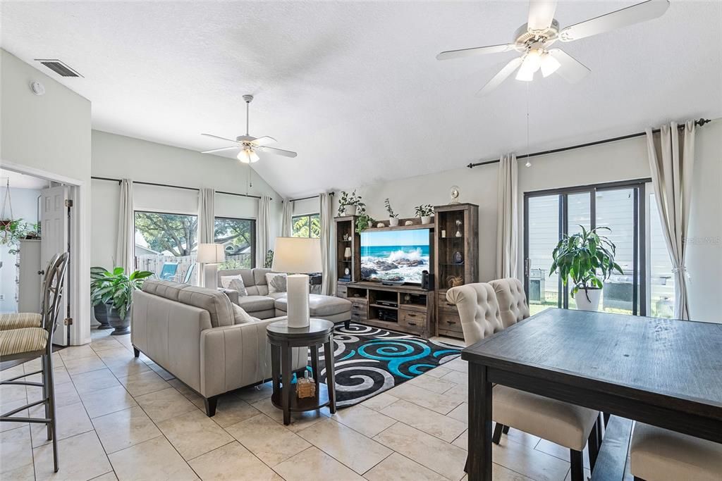 Photo of living room/dining room from the foyer.  Primary bedroom entrance in background to the left.  Back yard can be accessed by a trio of sliding glass doors.  Two from the living/dining rooms and one from the primary bedroom.