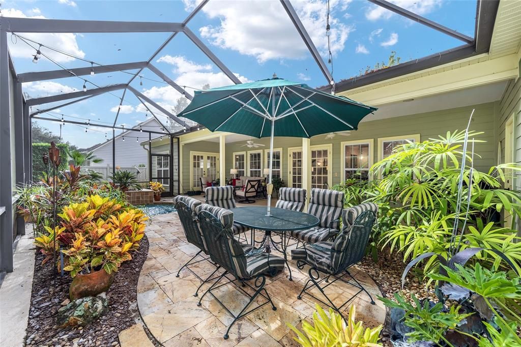 LOVELY LANDSCAPED BEDS AND TRAVERTINE PAVERS WEAVE THROUGH THE PATIO AREA