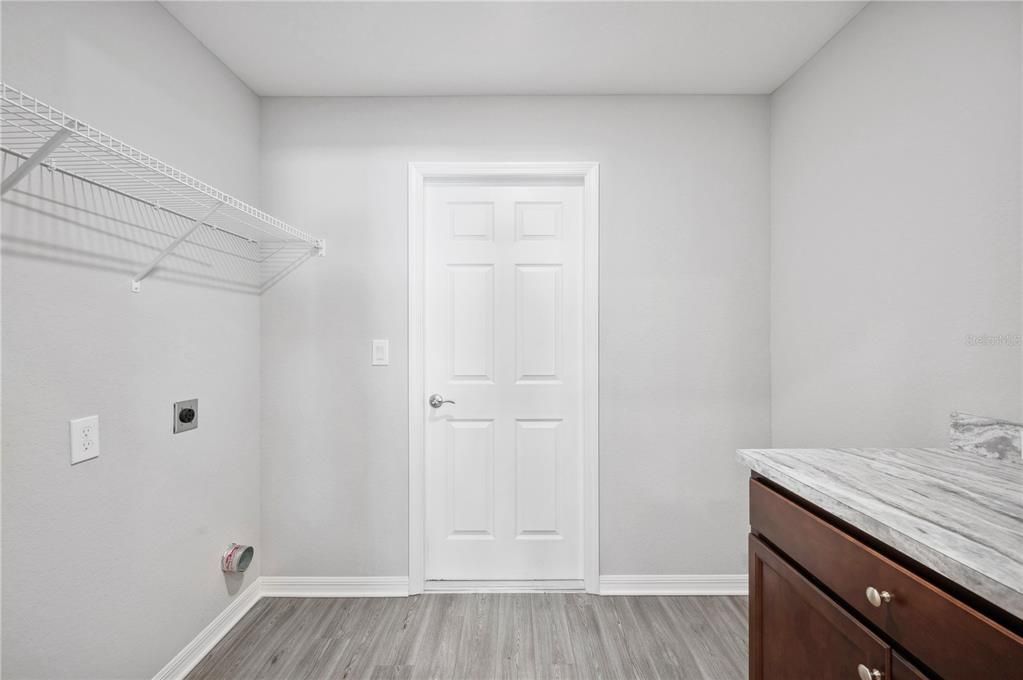 Laundry Room with door leading out to 2-car garage. Overhead shelving to left and Built-in Cabinet with Counter space to the right.