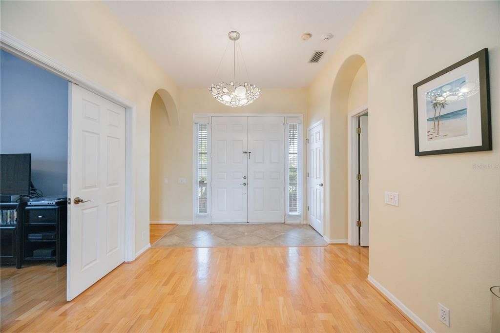 Gorgeous open foyer with front door side lights, polished hardwood flooring and timeless light fixtures