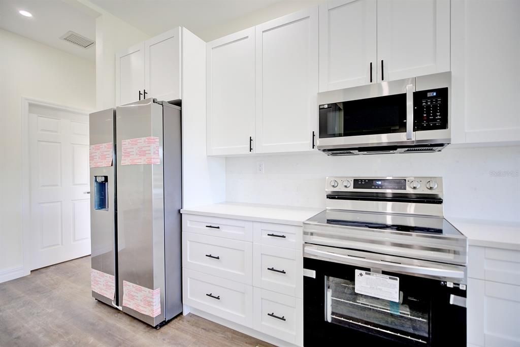 View of the kitchen toward the stove and refrigerator.