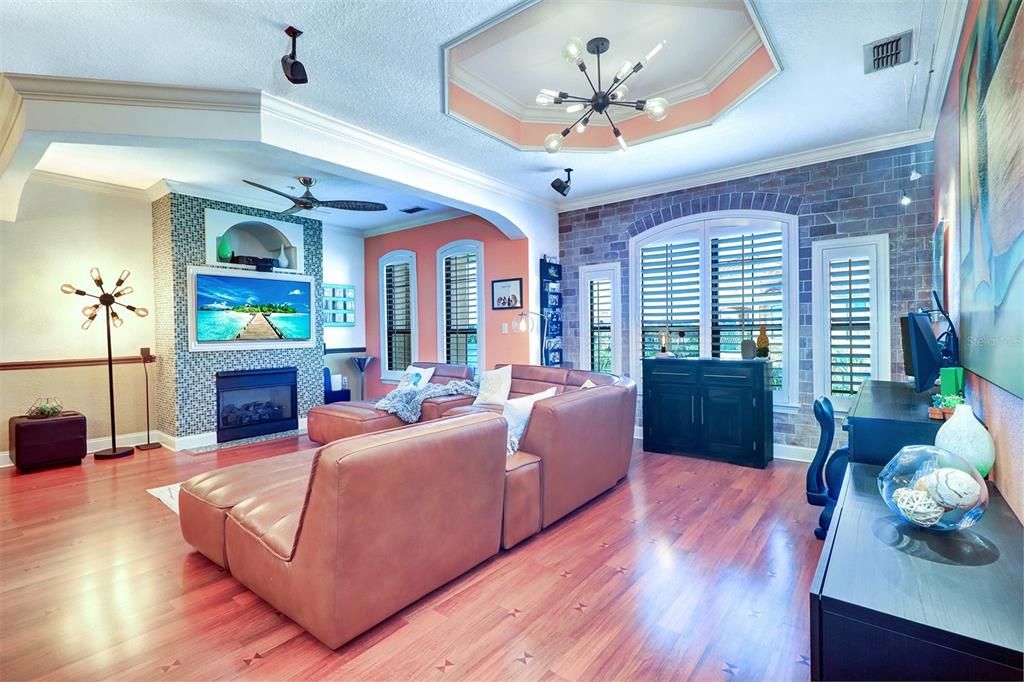 Large open living area from opposite living room wall viewing entertainment center with framed TV, gas fireplace & coffered ceiling with fan