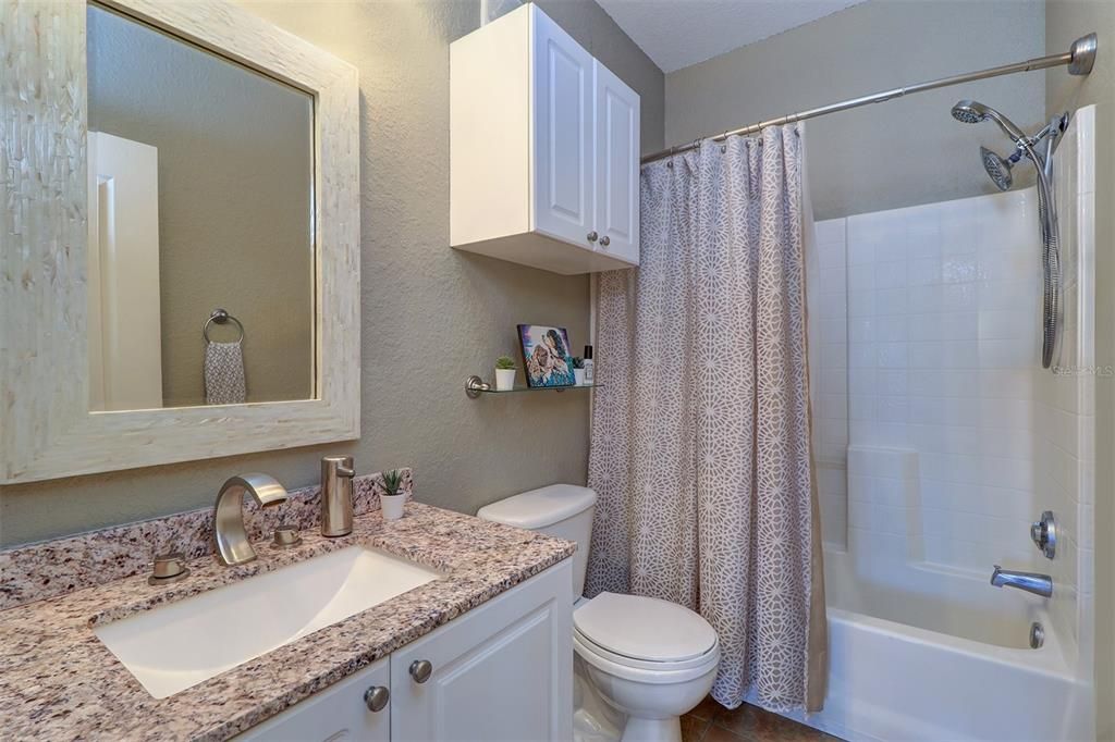 Guest/2nd bath has tub/shower combination, single vanity and cabinet, ceramic tile floor, brushed nickel faucet and showerhead