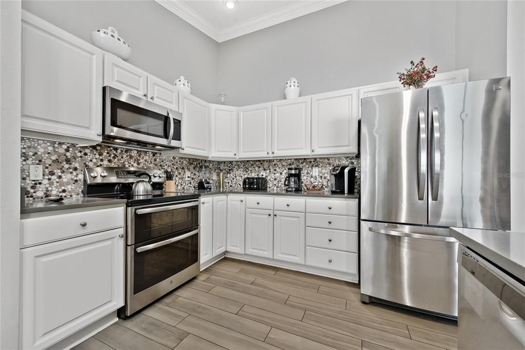 Under cabinet lighting showcasing beautiful marble backsplash. Stainless-steel appliances, double oven, many appliances for every day and special occasion use.