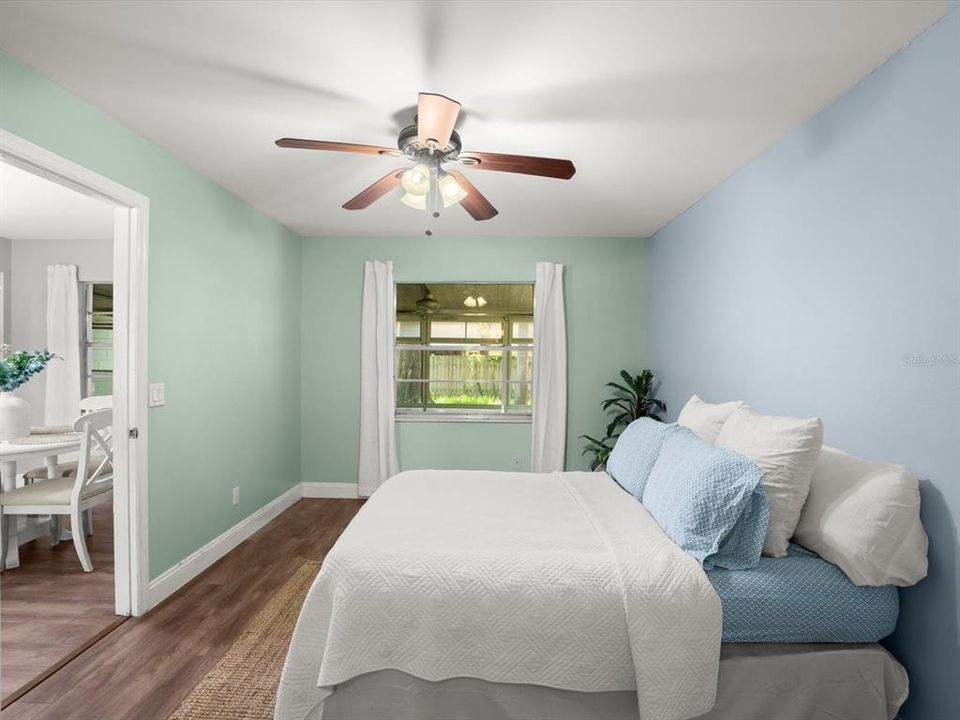 Primary bedroom off of the living and informal dining space. Primary bedroom has upgraded lighting with ceiling fan, large window overlooking the enclosed porch and an ensuite bathroom.