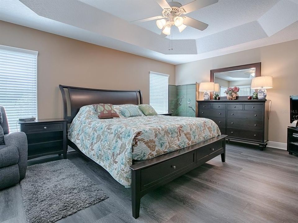 PRIMARY BEDROOM WITH LUXURY VINYL PLANK FLOORING AND TRAY CEILING.