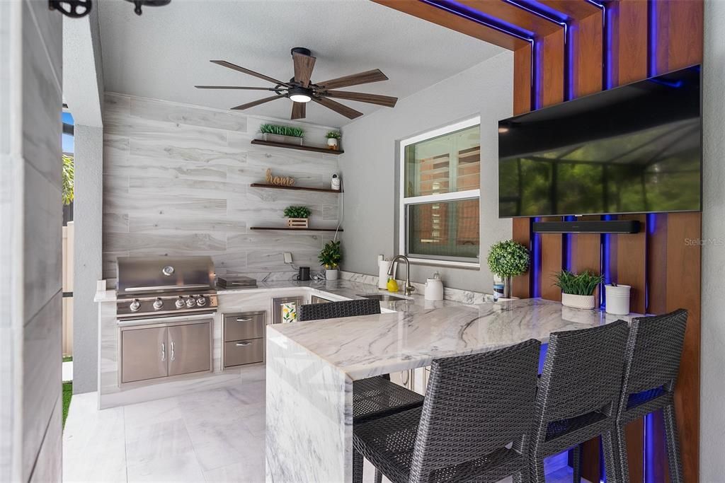 Outdoor summer kitchen with granite waterfall edge bar top seating area with custom LED lit wall