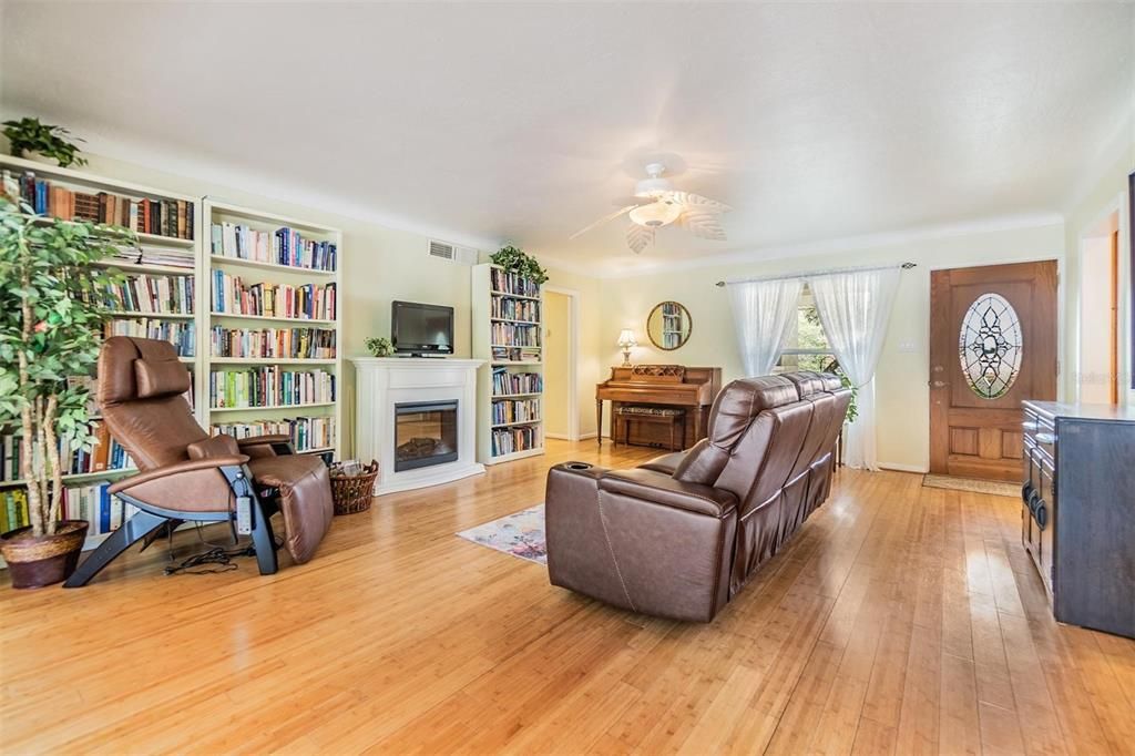 Living room facing the front door and doorway to guest bath and bedrooms. Designer fan, Natural wood flooring and coved ceiling for softened angles.