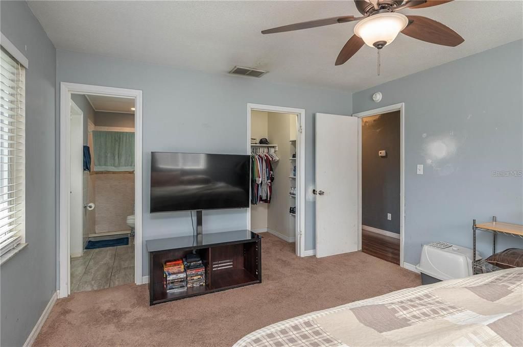 Primary bedroom showing walk-in closet, ceiling fan, and entry to primary bathroom.