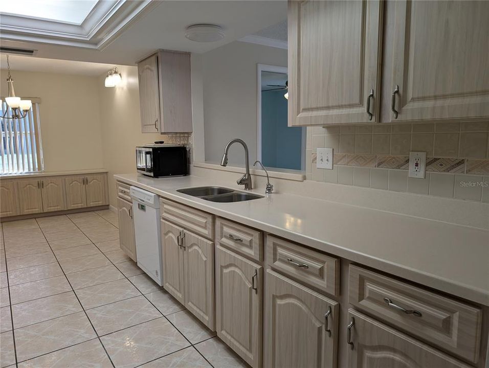 Dining room view of kitchen, pass thru window into Florida room with a glimpse of the 3rd bedroom.  Also visible is microwave, dishwasher and stainless steel sink.