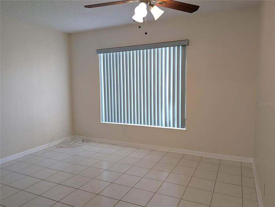 Guest bedroom is at opposite end of the hallway from the primary bedroom.  Features also include tile floor, ceiling fan and large window.