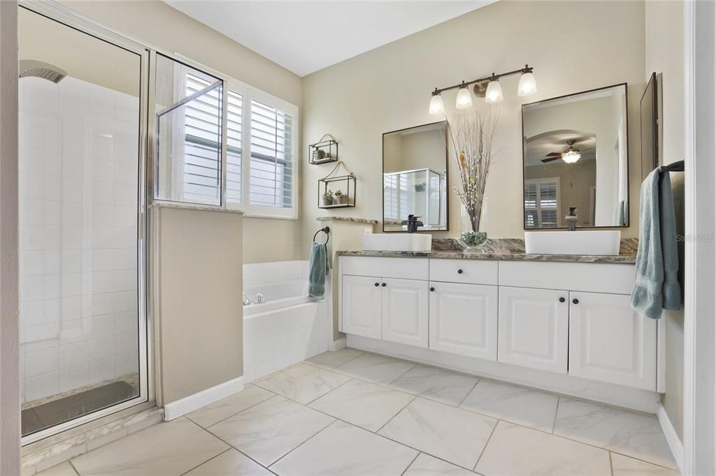 Updated 10' x 8'6" Primary Bathroom w/ ceramic tile, granite countertop w/ dual sinks, glass enclosed shower & corner tub