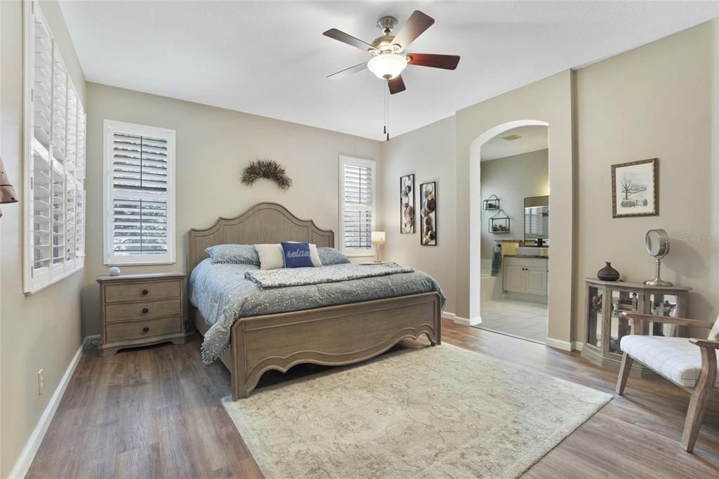 13' 6" x 16'6" Primary Bedroom w/ luxury vinyl floor, Plantation style shutters & a ceiling fan