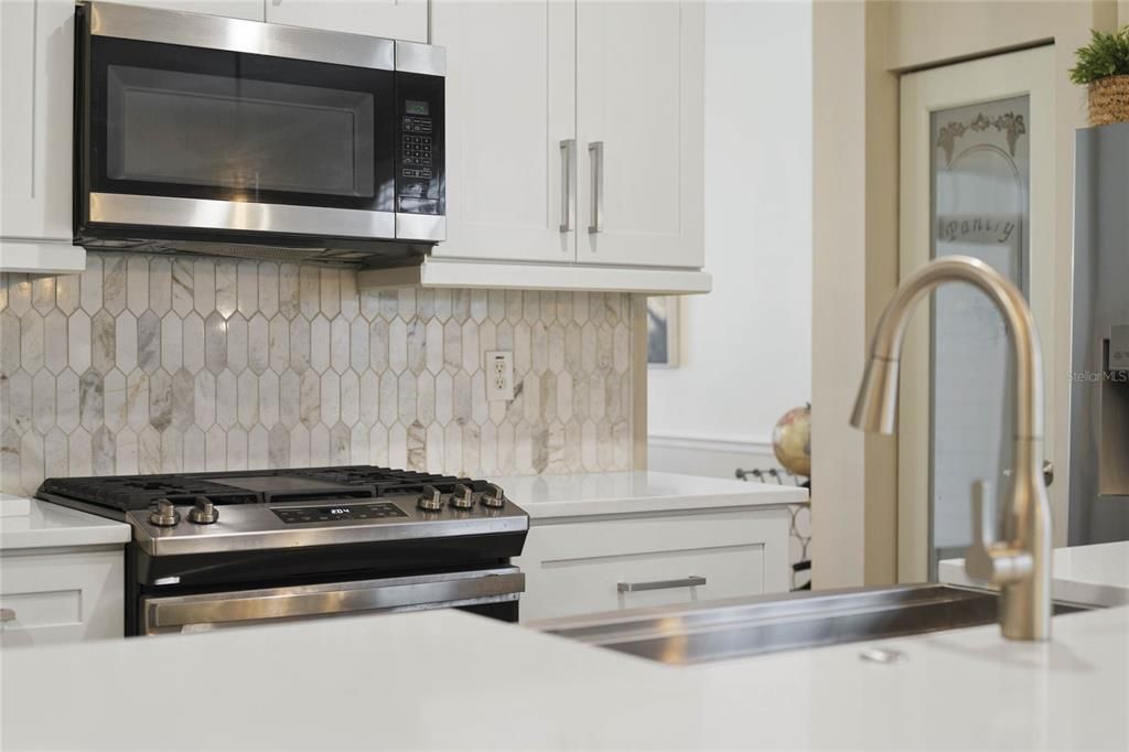 Kitchen w/ 5-burner natural gas range, stainless steel appliances, tile backsplash & farmhouse sink