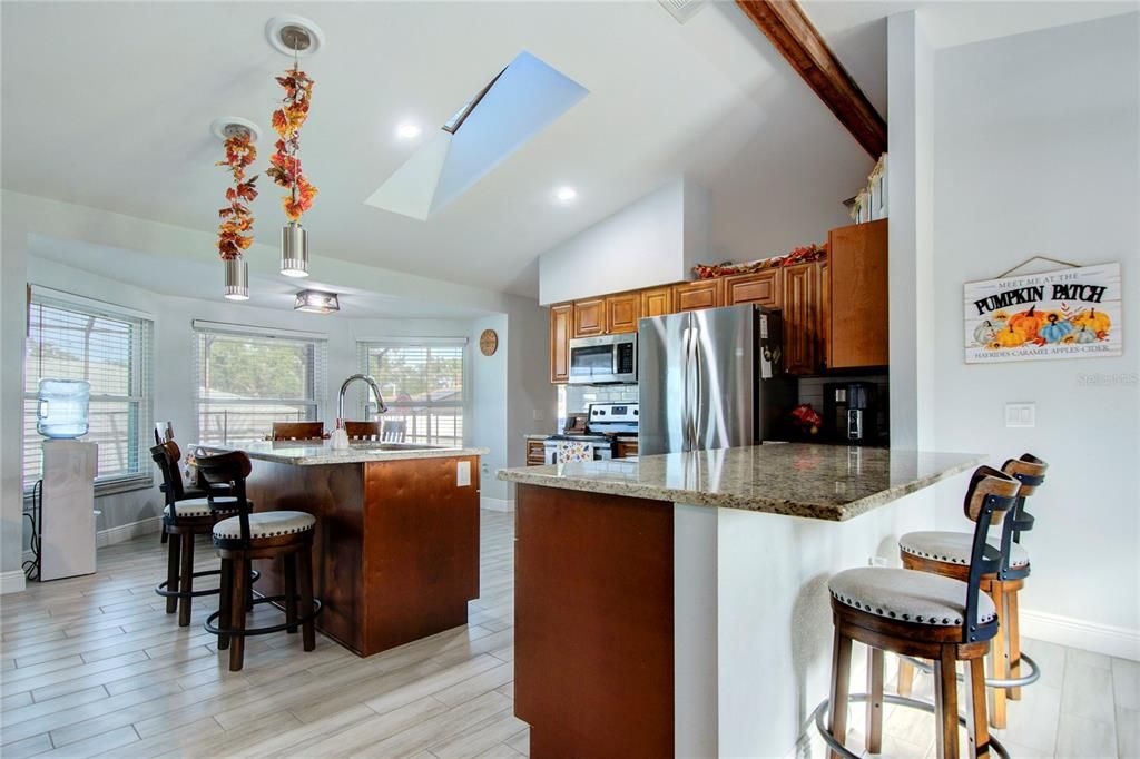 Open kitchen with vaulted ceiling, skylight, wood cabinets, granite countertops, and stainless steel appliances