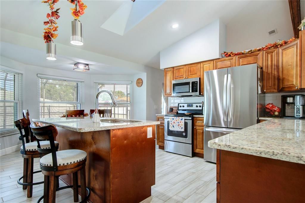 Open kitchen with vaulted ceiling, skylight, wood cabinets, granite countertops, and stainless steel appliances