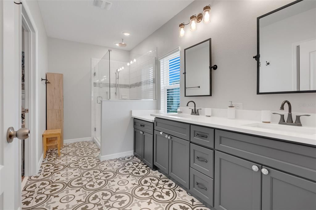 Primary bathroom showcasing dual sinks, sleek quartz countertops, elegant tile flooring, and a walk-in shower with multiple shower heads.