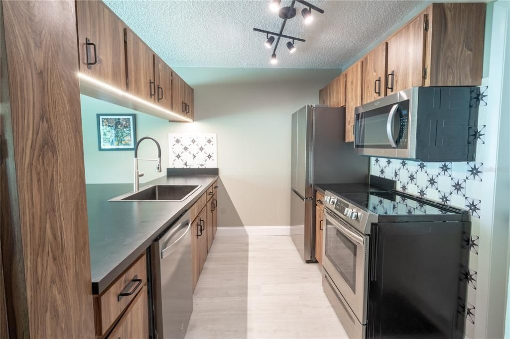 The kitchen features brand new appliances including a stainless steel SMART Samsung refrigerator with icemaker, microwave, glass-top range, dishwasher, countertop, sink and faucet.