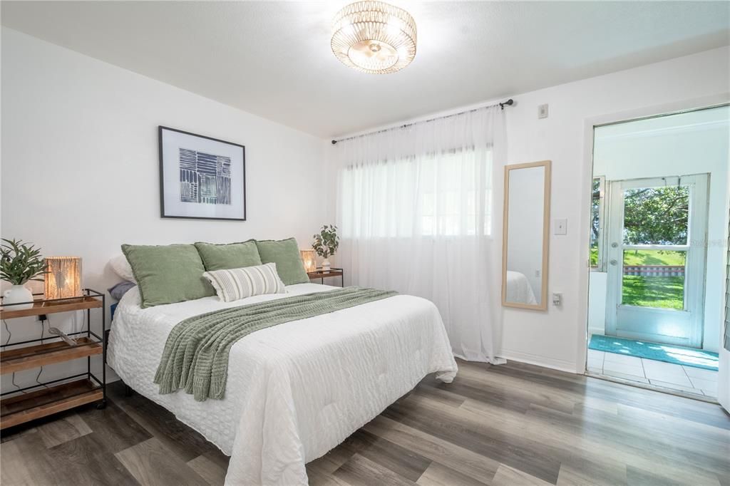 The primary bedroom is light and bright, featuring wood laminate flooring, a modern light and ceiling fan.