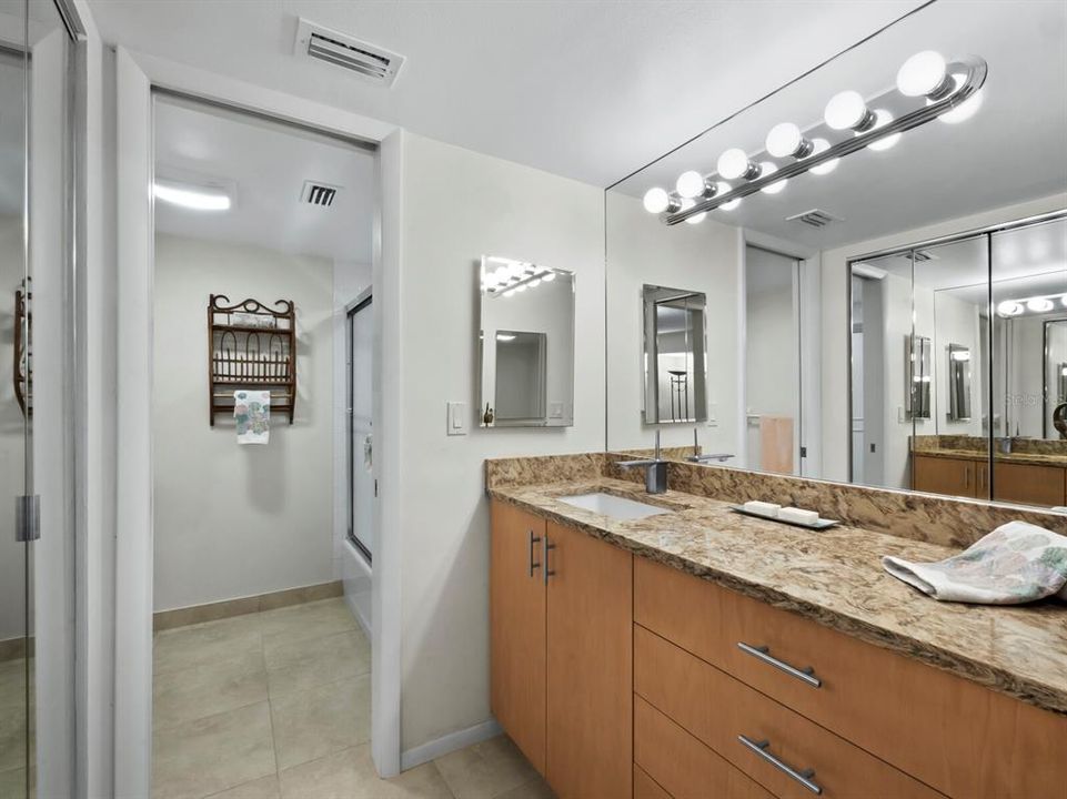 The ensuite bath features a separate vanity area with Hollywood lighting, wall-to-wall mirror, granite counters, solid wood cabinetry and a secondary built-in closet.