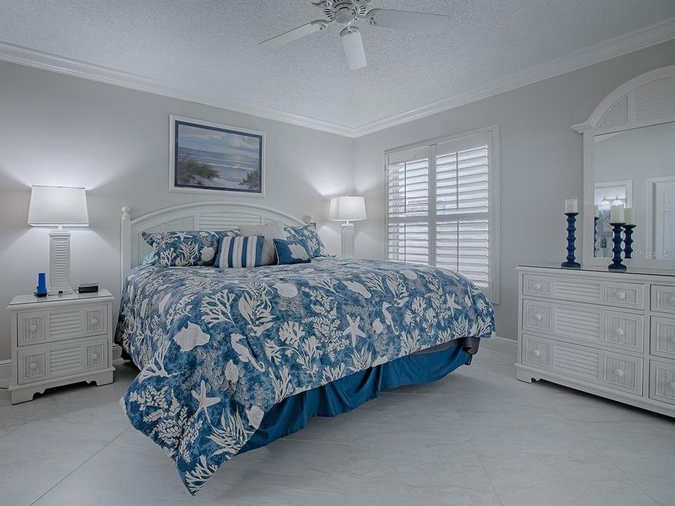 PRIMARY BEDROOM WITH DIAGONAL TILE, CROWN MOLDING, AND PLANTATION SHUTTERS.