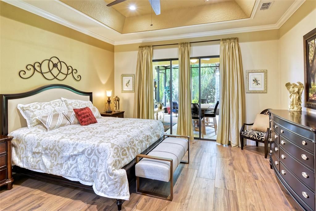 Primary bedroom with PORCELAIN wood-look TILE, TRAY CEILING, RECESSED LIGHTING, and TRIPLE SLIDER to the lanai, crown, and additional moldings to set this room apart