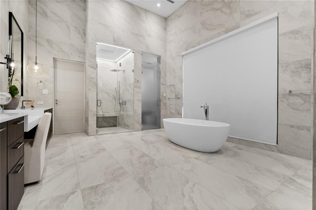 Master bathroom features 2 showers, 2 bathrooms, vanity with 2 sinks and a freestanding tub all tiled floor to 16 ft ceiling.