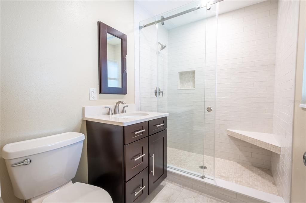 The primary bathroom features a mirrored vanity with storage, and a tiled walk-in shower with built-in shower bench and glass enclosure.