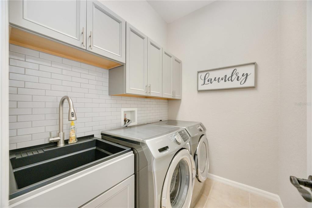 Utility room with large wash sink, washer/dryer, plentiful storage space and luxurious backsplash to complete the aesthetic of the utility room