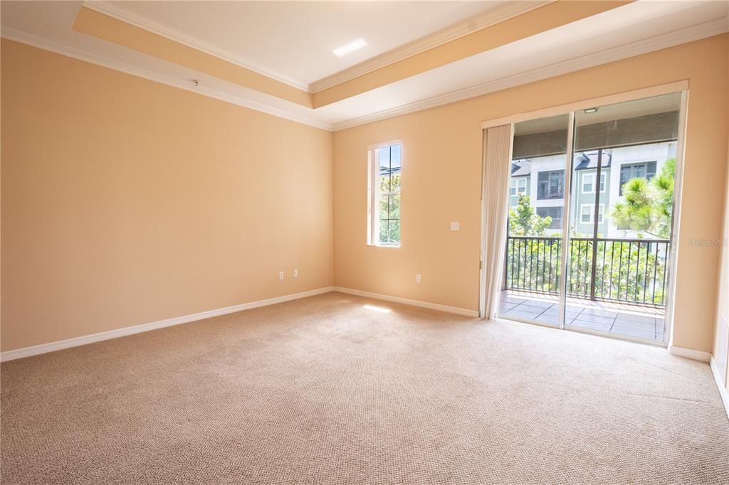 The primary bedroom features neutral tone carpet, crown molding, a tray ceiling and sliding glass doors that lead to a private balcony.