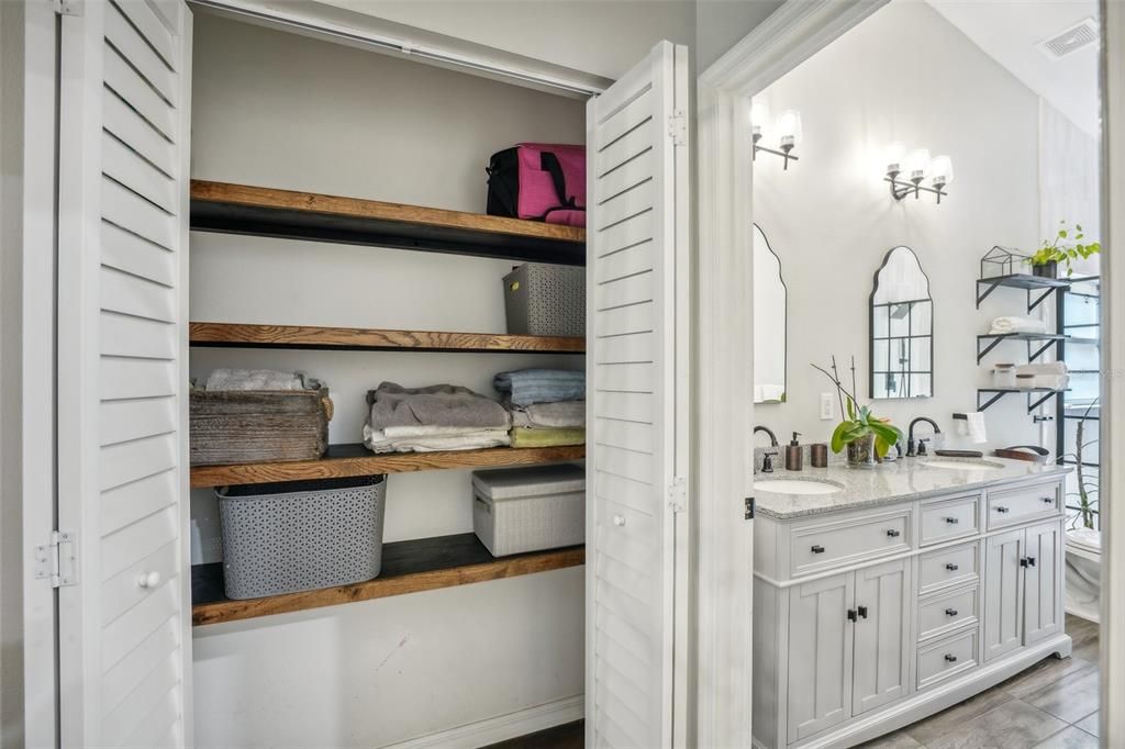 Linen closet with wood shelves between primary bathroom and bedroom