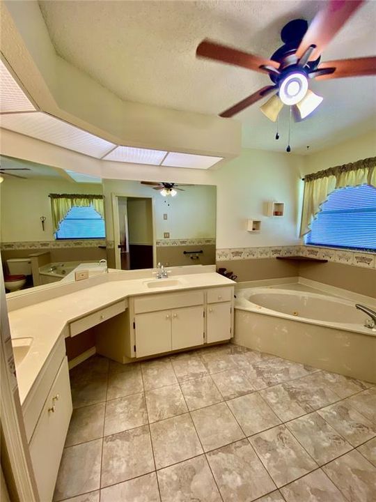 En Suite Primary Bathroom with Dual Sinks, Vanity Area, Whirlpool Bath Tub...Linen Closet, Neutral Tile Floor, Lighted Ceiling Fan