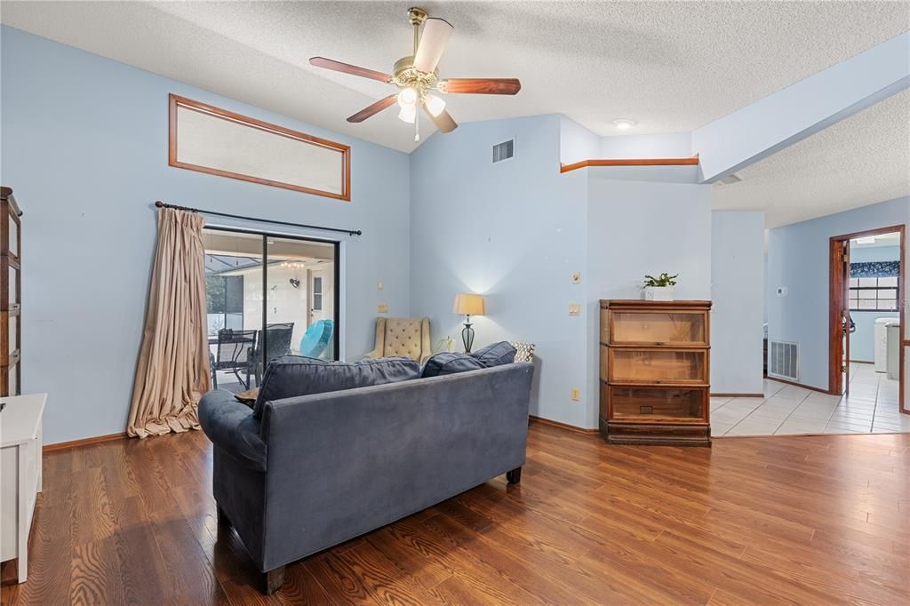 Family Room off the front foyer featuring vaulted ceilings, wood floors, and a sliding glass door to the back lanai.