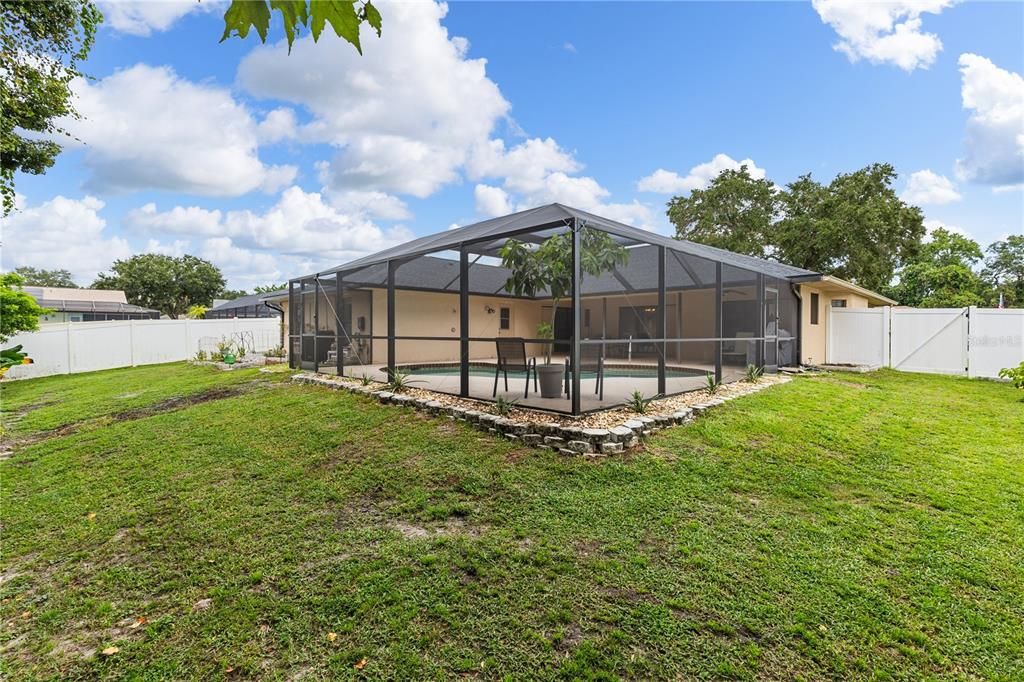 Fenced-in back yard featuring several fruit trees, fruit plants, and two raised planters.