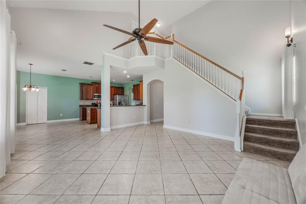 Great room with cathedral ceiling with view of kitchen area and open staircase.