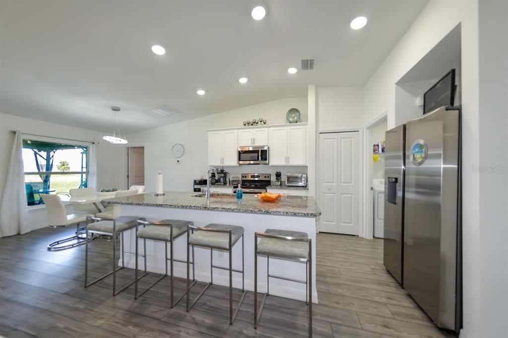 Kitchen featuring an island with sink, touchless faucet, white cabinetry, vaulted ceiling, luxury vinyl wood-style flooring, and stainless steel appliances