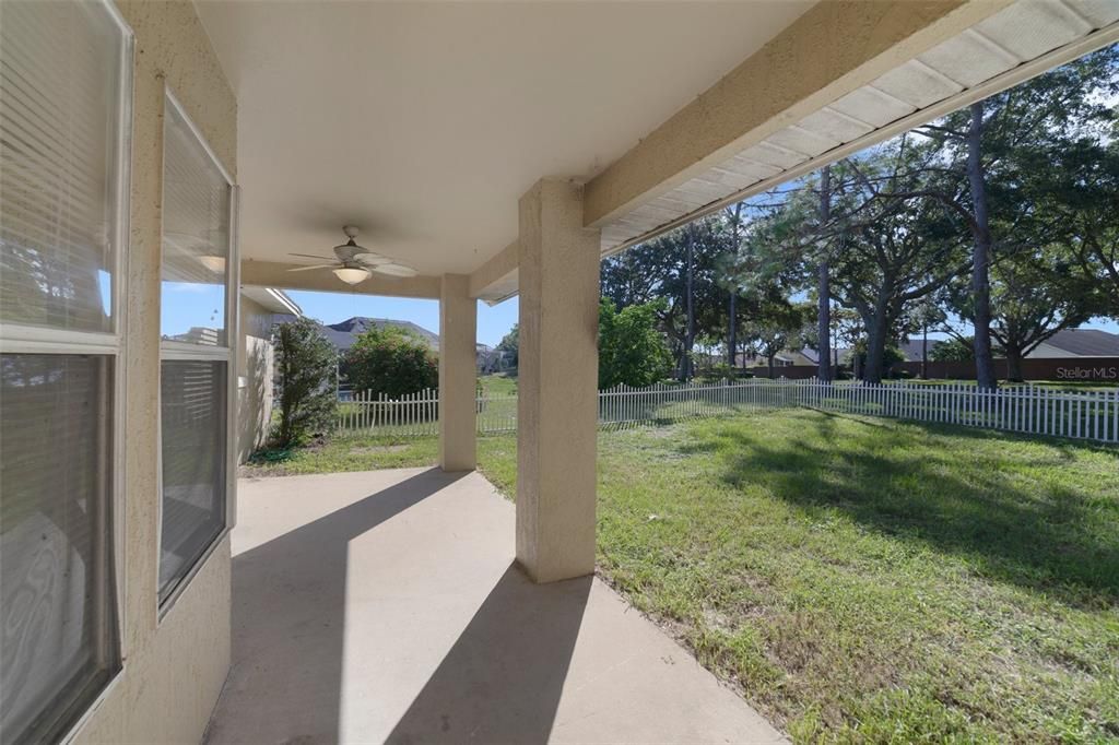 Outside a COVERED LANAI overlooks a fenced backyard and lovely mature trees to host family and friends or relax and unwind at the end of a long day.