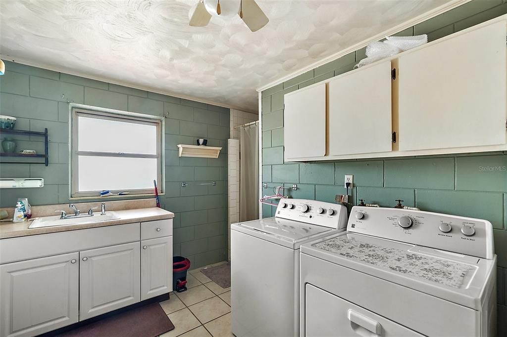 Expansive laundry room features washer, dryer, storage space, laundry sink, & walk-in shower