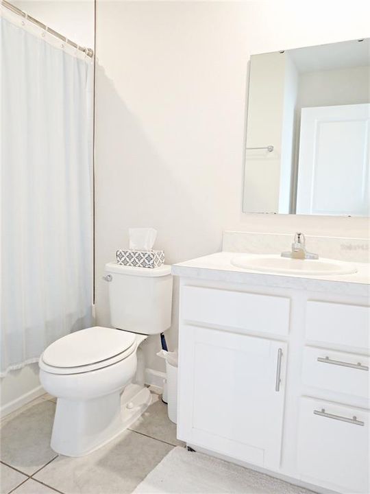 Guest bathroom has a combination tub/shower, white cabinets and tiled flooring.