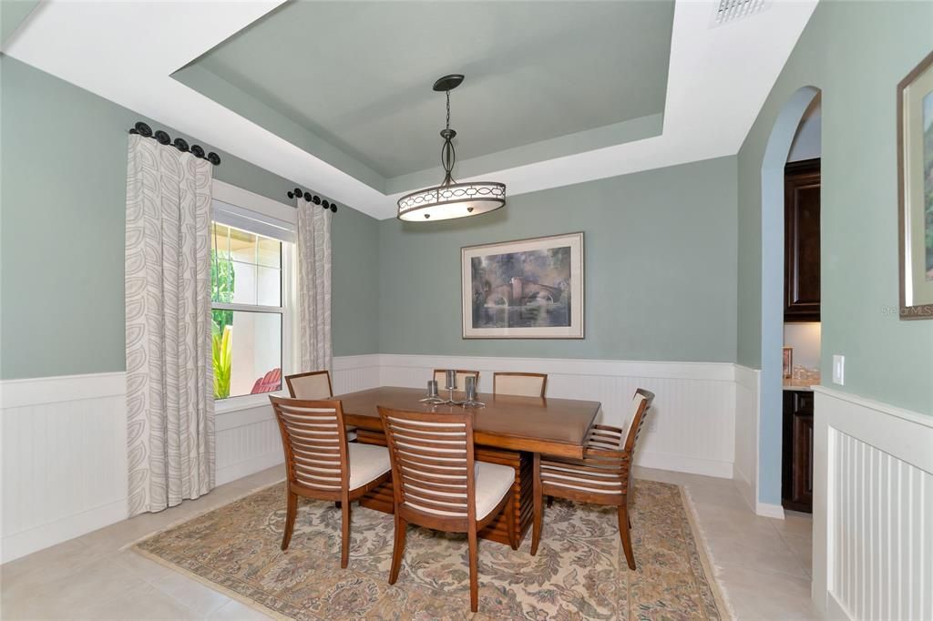 Dining room with stepped ceiling, butler's pantry, & impact glass front window.