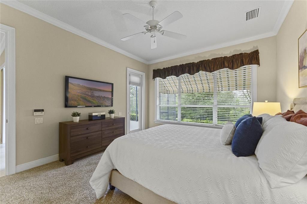 View of the Primary Bedroom w/ glass door to screen enclosed covered patio overlooking the conservation area