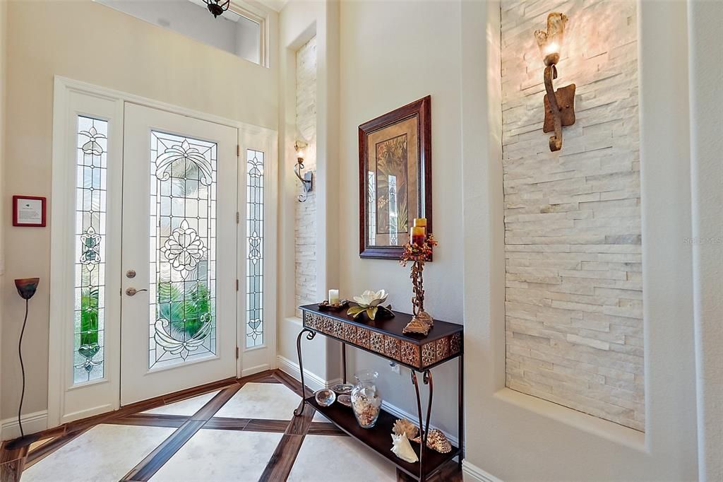 Elegant Quartzite wall inlay with pretty scones plus beautiful artistic glass front door and sidelights.