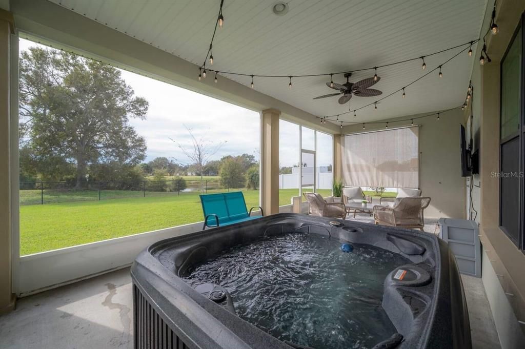 Screened Lanai with private 5-person hot tub, outdoor TV, and serene views of the large fenced yard and pond.