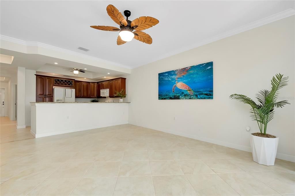 Living room with ceiling fan, light tile patterned flooring, and ornamental molding